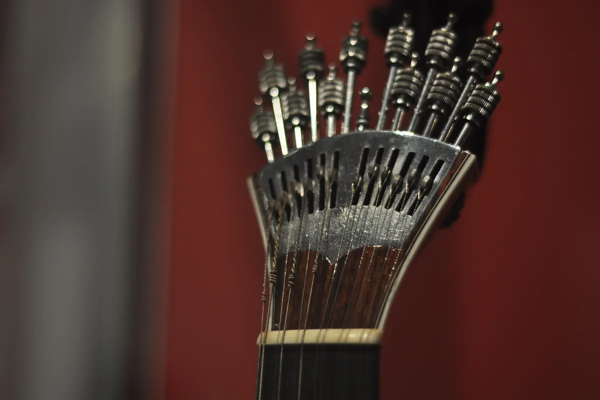 Vista de perto das cravelhas metálicas de uma guitarra portuguesa sobre um fundo vermelho