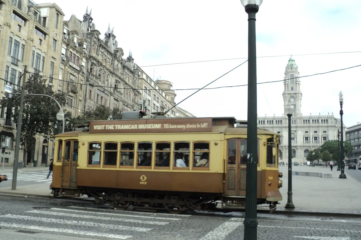 Eine historische Straßenbahn auf einer breiten Avenue in Porto, dahinter der Turm des Rathauses